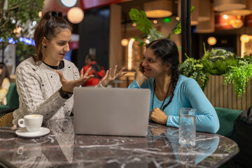 Women friends discussing ideas using laptop in cafe