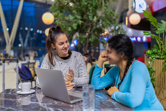 Women travelers collaborating on laptop in airport lounge
