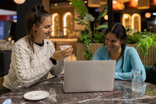 Women smiling, collaborating on laptop in cafe - Powered by Adobe