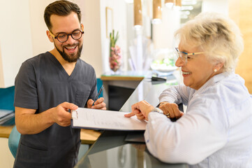 Male ophthalmologist handing medical form to senior woman at reception counter during her hospital appointment