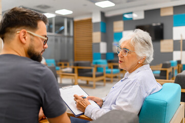 Senior woman discussing her medical records with male ophthalmologist while sitting in the hospital waiting room