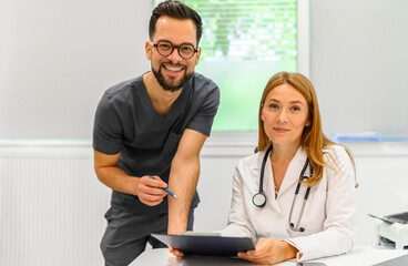 Portrait of confident male and female doctors discussing medical records and collaborating at hospital desk