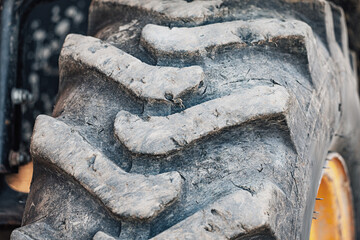 Large, grubby tractor tire featuring worn rubber tread patterns and a yellow wheel rim, ready for...