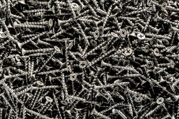 Many black metal self tapping screws for construction work, closeup, top view. New metal fasteners self tapping screws for connecting wooden elements. Background and texture of metal screws