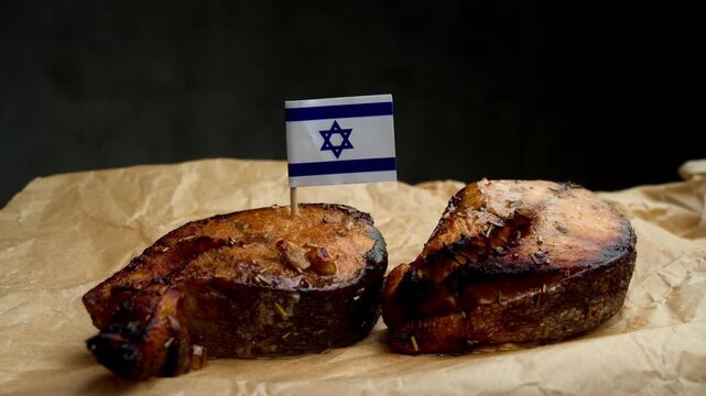 Close up of grilled fish steak with Israeli flag on skewer, scene emphasizes local Mediterranean fishery and kosher seafood production.