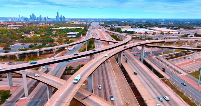 Footage over the complex multi-level interchange in the big city. Cars run to and from the city downtown at daytime. Aerial view.