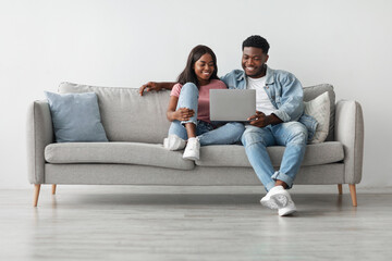 Happy loving young African American couple using pc, watching video, looking at their photos or...