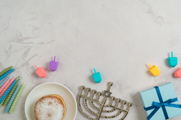 Jewish holiday Hanukkah concept with traditional donuts, menorah, colorful candles and gift box on bright background. Top view, flat lay