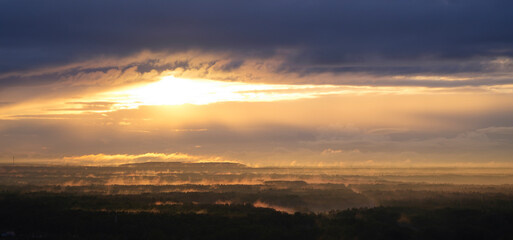 Sunlight rays through dark clouds in the morning at dawn with fog creeping over the forests