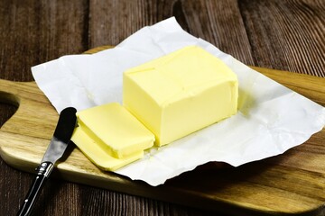 Real butter on wooden cutting board with knife.