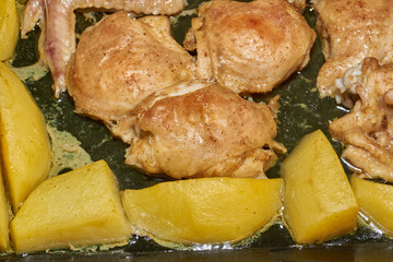 Oven-baked chicken pieces with potato slices and seasoning mixture. Close-up.