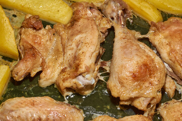 Oven-baked chicken pieces with potato slices and seasoning mixture. Close-up.