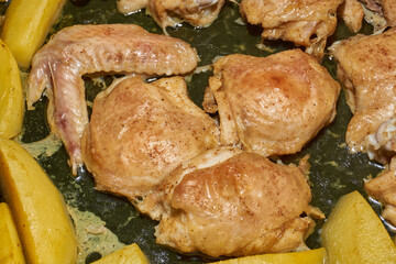 Oven-baked chicken pieces with potato slices and seasoning mixture. Close-up.