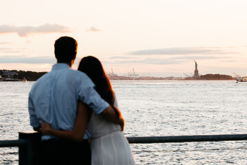 Fototapeta premium Romantic Couple Looking Toward Statue of Liberty at Sunset