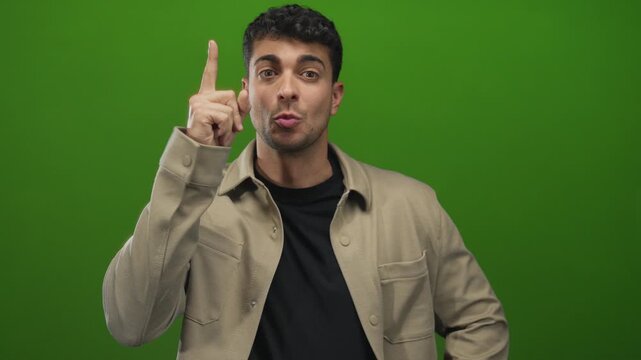 Man touches chin while thinking against a background showing a young hispanic guy in a green studio pondering.