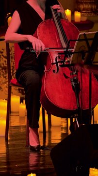 A female cellist performs on stage, her hand poised on the cello s neck, surrounded by softly glowing candles that set a warm atmosphere