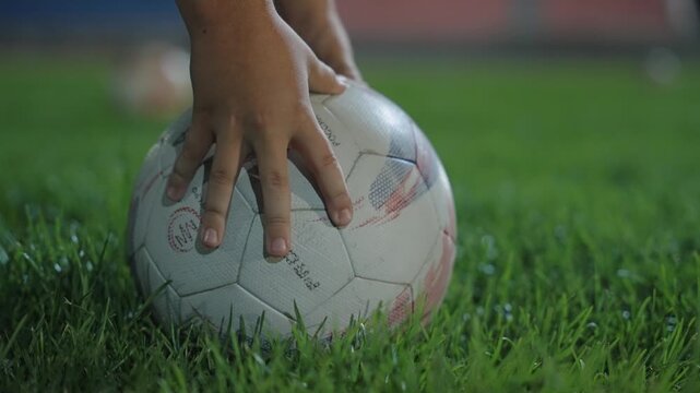A footballer's hands place the ball on the turf of a football field before a shot