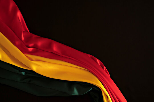 Black History Month background. Red, yellow, green colors drapery, silk flag on black background. Top view
