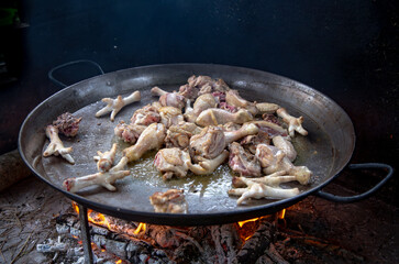 Traditional Valencian paella cooking process: frying chicken pieces in hot oil – Mediterranean cuisine in Spain.