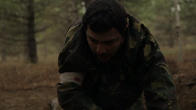 Exhausted soldier in camouflage uniform crawls and collapses on the forest ground. Injured military man falls face down in dirt during combat, depicting struggle, pain, and defeat.

