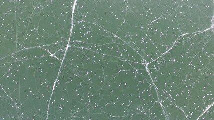 Aerial view of frozen lake surface with thick ice layer and cracks in a northern polar region. The icy terrain reveals fractured patterns across the solid frozen water sheet in the high latitude zone. - Powered by Adobe