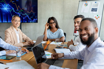 Group of coworkers from diverse backgrounds smile and pose together in a bright office during a corporate meeting. They are engaged in teamwork and look happy at their workspace.