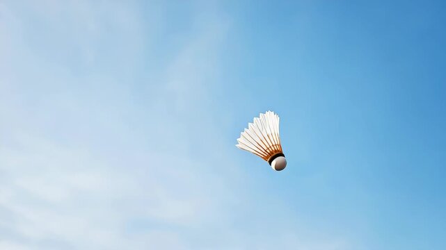 A white badminton shuttlecock is flying in the air. The shuttlecock is white and has a black stripe