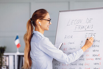 A teacher conducts a French language lesson in a modern classroom. She writes on a whiteboard while...