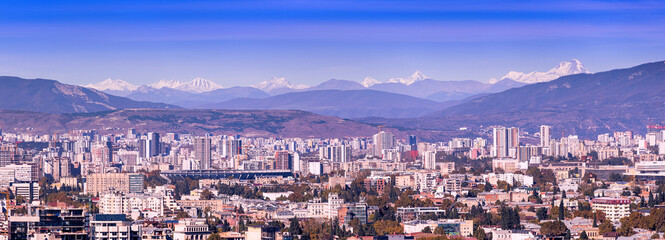 Tbilisi, Georgia urban cityscape panorama presenting the modern city buildings against the majestic snow capped Caucasus Mountains