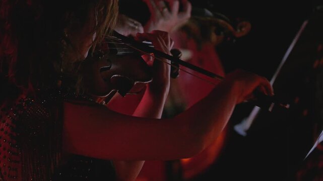 A close-up of a violinist's hand skillfully playing the violin, with dramatic lighting highlighting the elegant movements of her hands