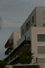 Fototapeta premium row of terraces and balconies in modern grey block, crisp horizontal lines with small trees below, industrial minimalism meets neighborhood calm, late light softening concrete edges and metal details