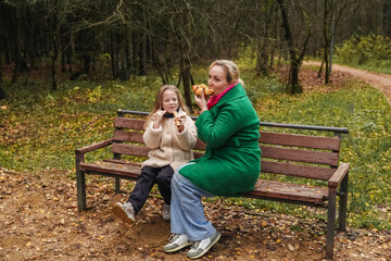 Fototapeta premium Sitting mother with daughter on park bench. Family talk, smile supports love, care, trust. Outdoor rest during walk adds bonding, childhood happiness, motherhood lifestyle, weekend leisure, comfort.