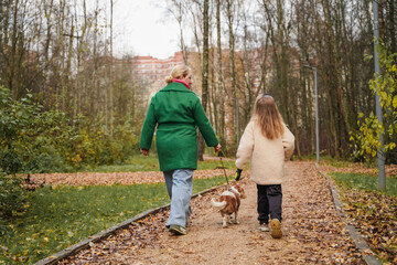 Fototapeta premium Walking mother with daughter, dog on park path. Family pet activity supports bonding, care, safety, healthy exercise. Outdoor weekend stroll with small canine fits city lifestyle, childhood joy.