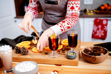 Woman preparing hot mulled wine in christmas and new year kitchen stirring aromatic mix of citrus...