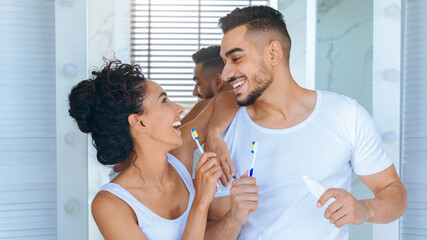 A happy couple shares a light moment while brushing their teeth in a bright bathroom. They are engaged in playful conversation, highlighting their connection and morning routine.