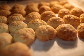 Close-up of golden, freshly baked cheese puffs resting on parchment paper on a baking sheet, illuminated by warm, intense light from above