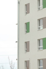 Apartment facade closeup showing green panels and windows with stucco finish, subtle security cameras and distant bare branches under overcast sky, clean geometry and muted color palette ideal