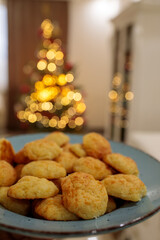 Appetizing plate of golden, freshly baked cheese puffs  on a blue rimmed plate, set against a blurry, warmly lit Christmas tree backdrop