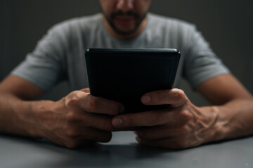 Cropped shot of man using e-reader device. Engrossed in reading ebook. Focusing on digital literature and online learning content. Concepts of concentrated study and modern education technology.