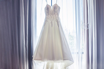 White wedding gown dress hanging against a window backdrop