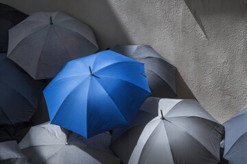 A striking blue umbrella contrasts against muted gray umbrellas, captured in a dynamic urban setting with shadows playing across the scene, creating a mood of resilience and protection