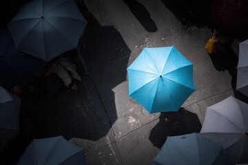 A striking blue umbrella contrasts against muted gray umbrellas, captured in a dynamic urban setting with shadows playing across the scene, creating a mood of resilience and protection