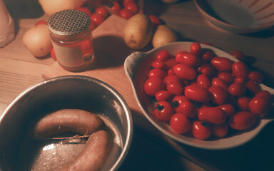 Sausages in the pan and dish with ripe tomatoes, kitchen table by evening, detail