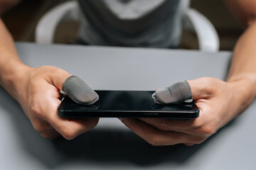 Close-up male hands wearing conductive finger sleeves on thumbs holding smartphone, improving touch screen sensitivity and grip for competitive mobile gaming and e-sports.