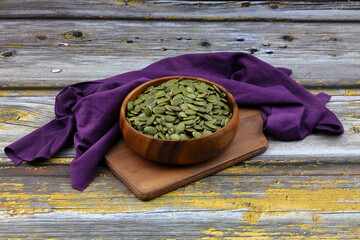 Pumpkin seeds in a wooden bowl on a wooden background