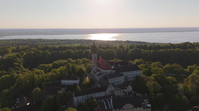 Drone footage of Kloster Andechs on Holy Mountain in Upper Bavaria, Germany. View of monastery, baroque church, lake Ammersee and green countryside near Munich at golden hour. Luftbild Heilige Berg. 