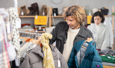 Stylish man standing in modern clothing shop and looking new down jacket made of high-quality...