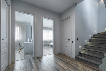 A modern home interior featuring an elegant hallway with stairs and rooms illuminated by natural light during the day.