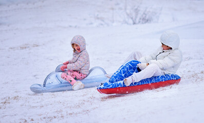 Joyful Children Sledding on Inflatable Sleds During Snowfall &ndash; Winter Fun, Outdoor Play, and Active Childhood Moments