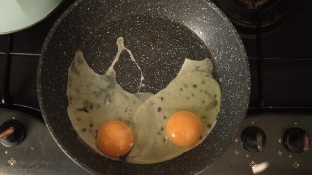 Close-up. Camera from above. In a frying pan in boiling oil, fried egg white. Two large chicken eggs are broken on the edge, in the afternoon in the apartment. Dirty, greasy gas stove, kitchen